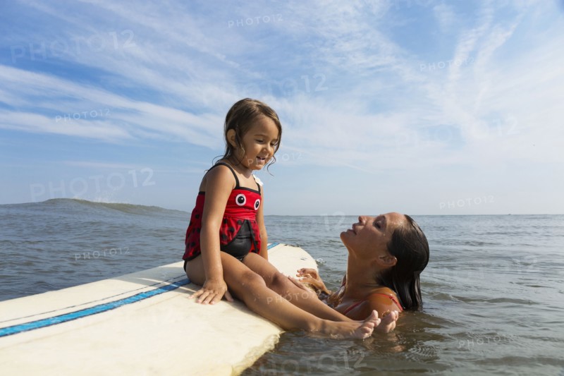 Mother teaching daughter to surf in ocean