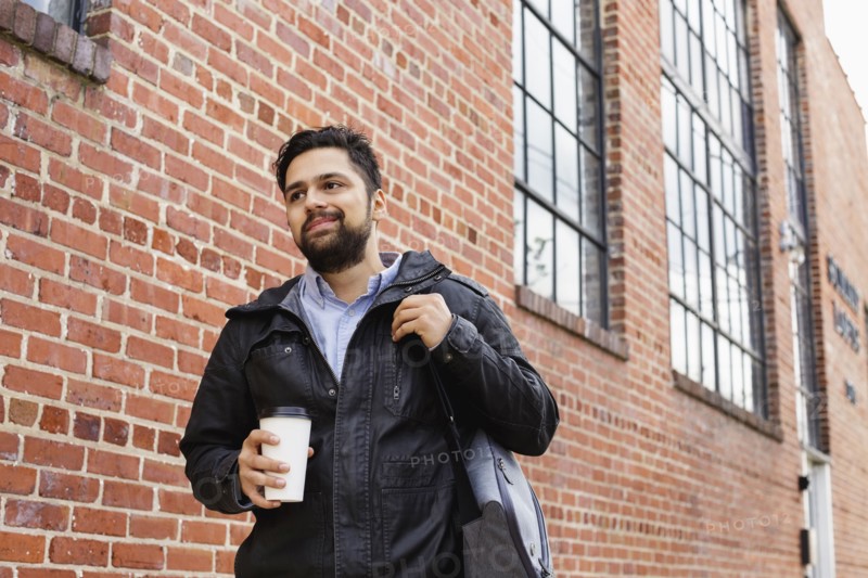Hispanic man carrying bag and coffee cup in city