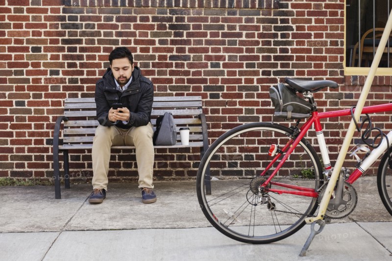 Hispanic man sitting on city bench using cell phone