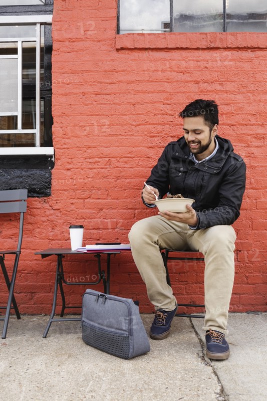 Hispanic man eating bowl of food on sidewalk
