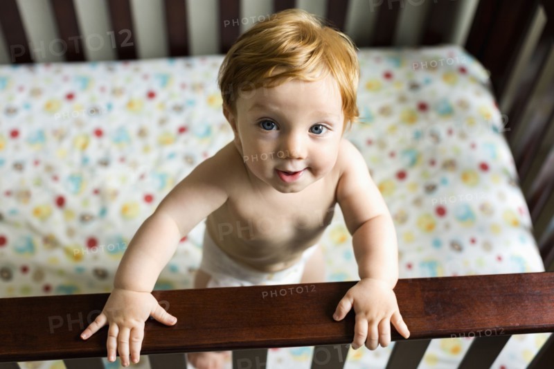 Portrait of curious Caucasian baby boy standing in crib