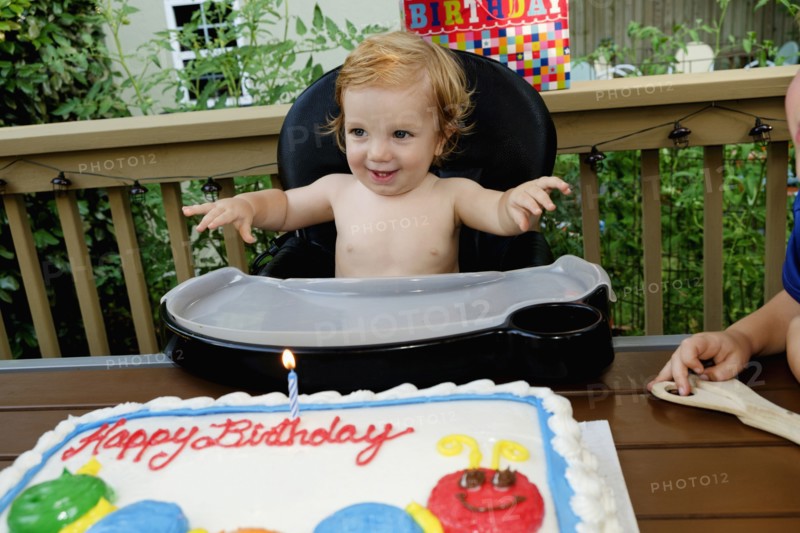 Caucasian baby boy in high chair near birthday cake