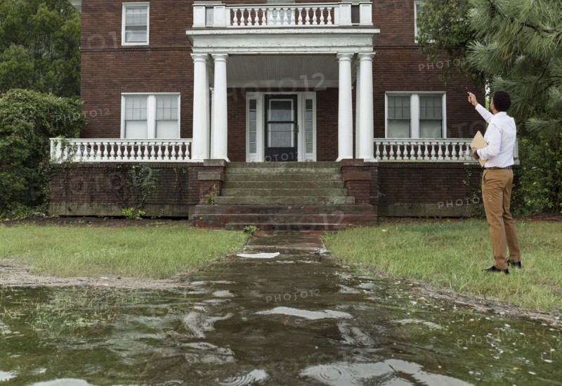 Black insurance adjuster examining flooding damage to house