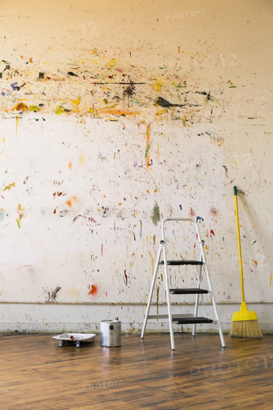 Paint splattered on wall near ladder and broom