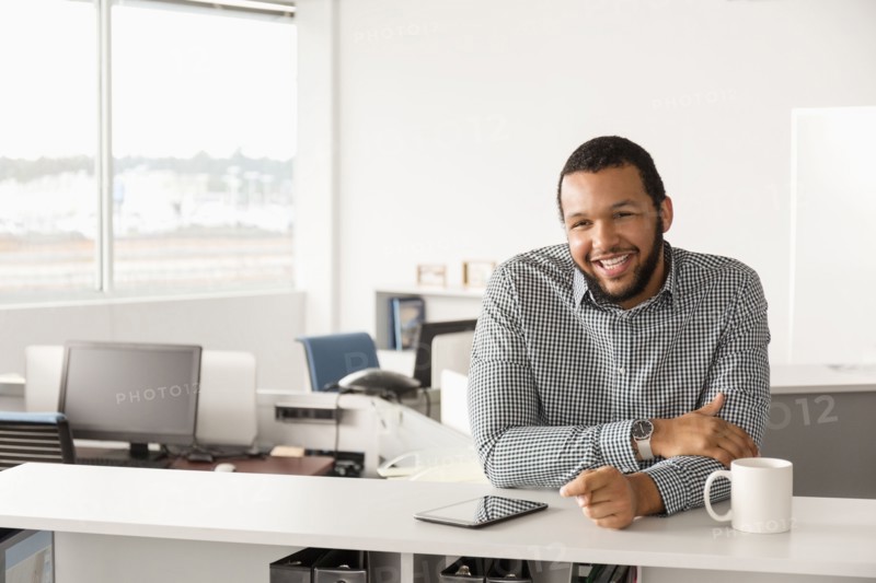 Smiling Mixed Race man leaning in office