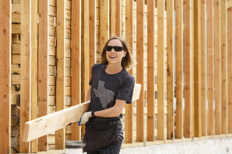 Caucasian woman carrying lumber at construction site