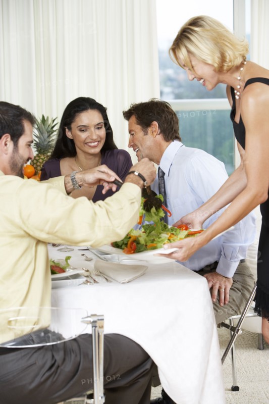 Woman serving friends salad at dinner party