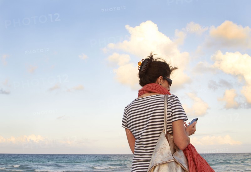 Caucasian woman holding cell phone on beach