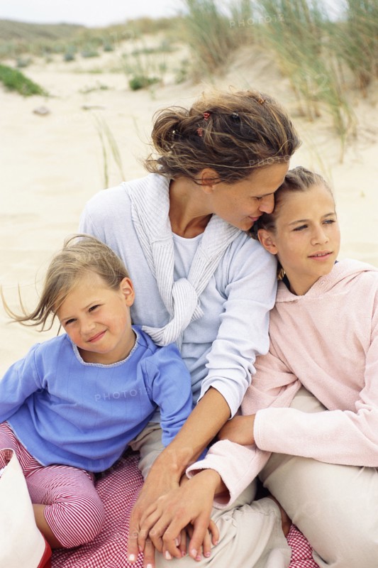 Caucasian mother and daughters hugging on beach
