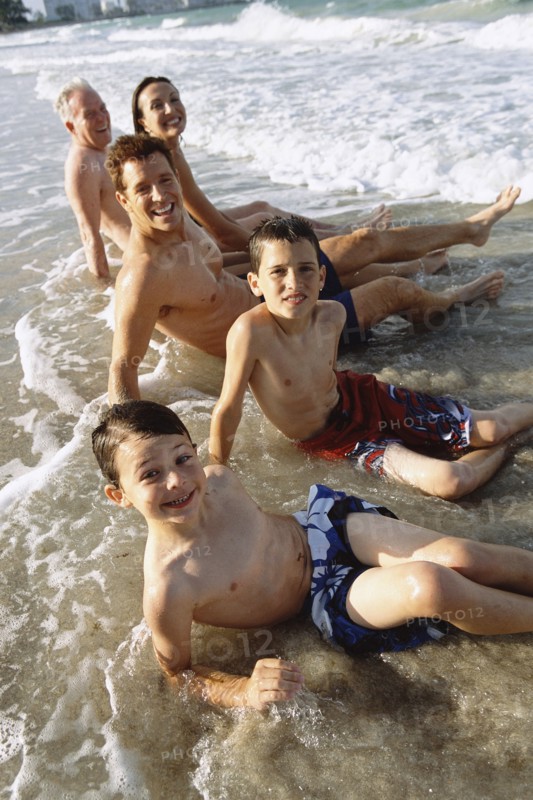 Family sitting in waves on beach
