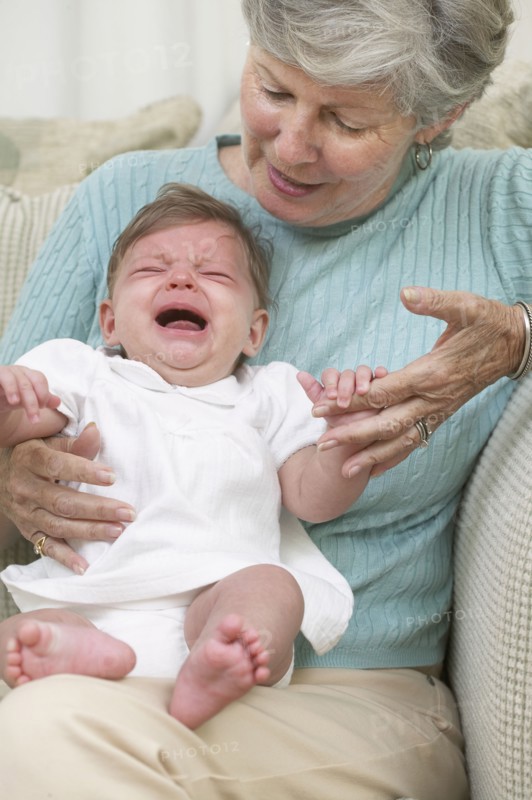 Senior woman with crying granddaughter on sofa