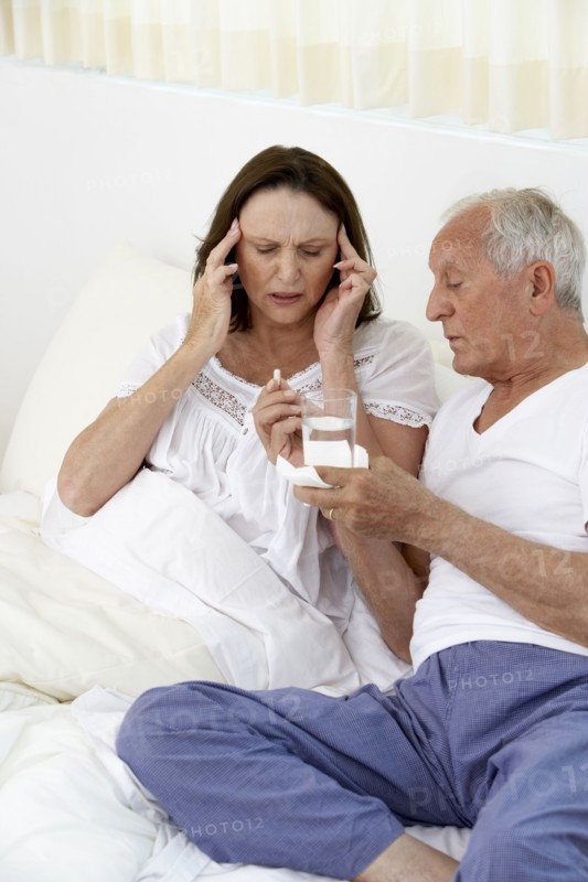 Senior man giving wife painkillers in bed