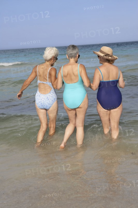 Senior women walking in waves on beach