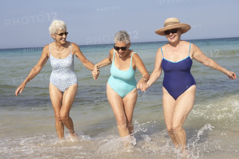 Senior women walking in waves on beach