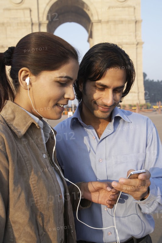 Indian couple listening to headphones by monument