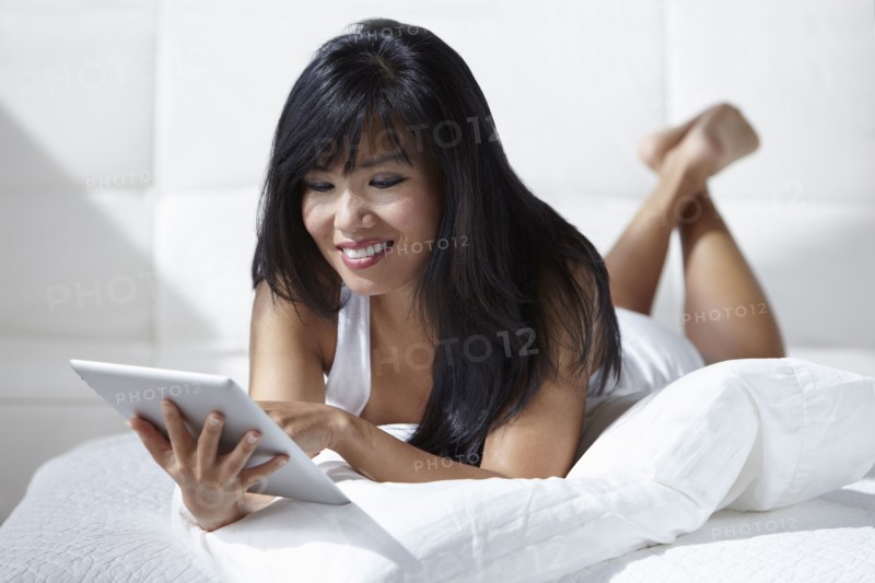 Woman laying on bed using digital tablet