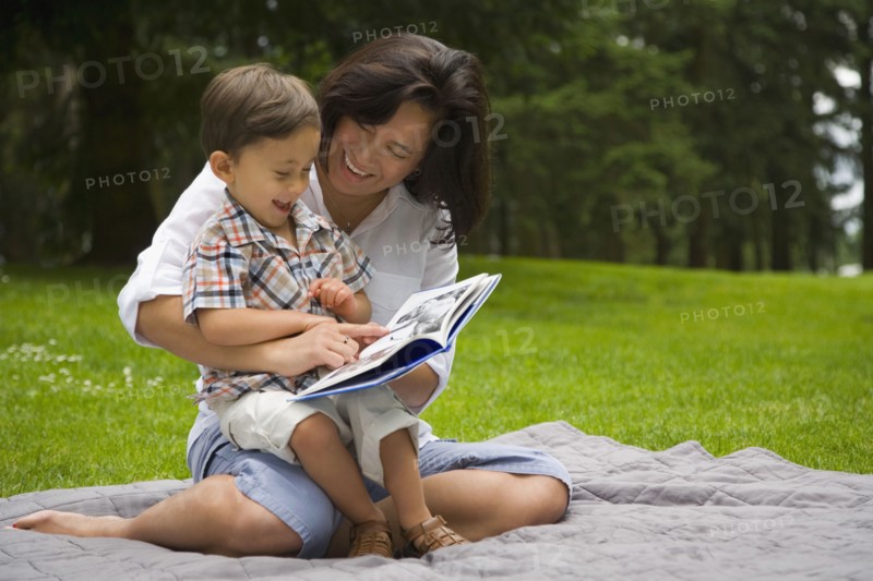 Boy reading story book in park with mother
