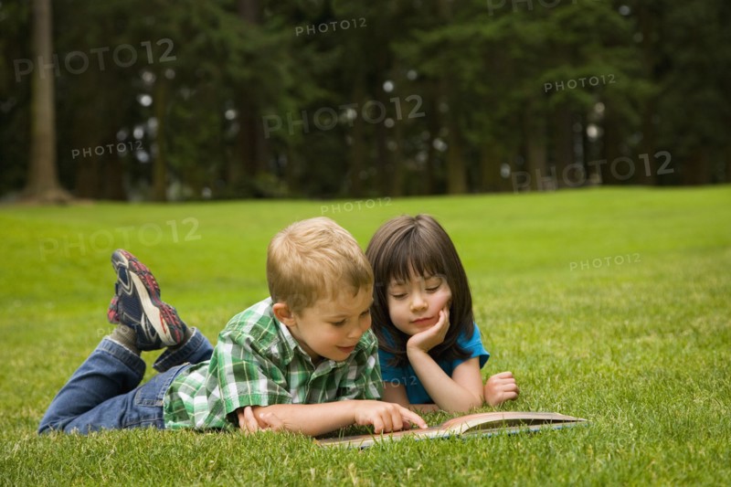 Brother and sister reading story book in park