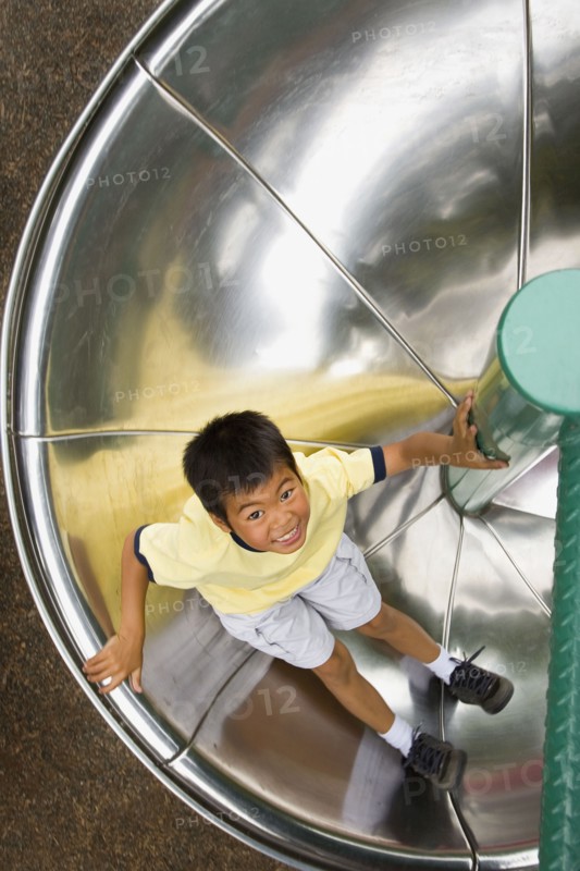 Asian boy sliding down circular slide