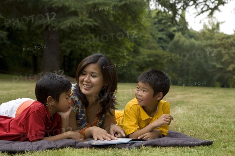 Asian mother reading book to sons in park