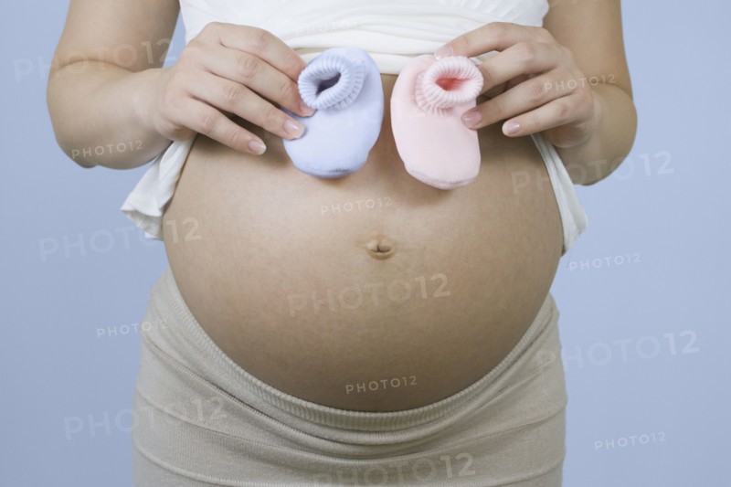 Pregnant Chinese woman holding pink and blue booties