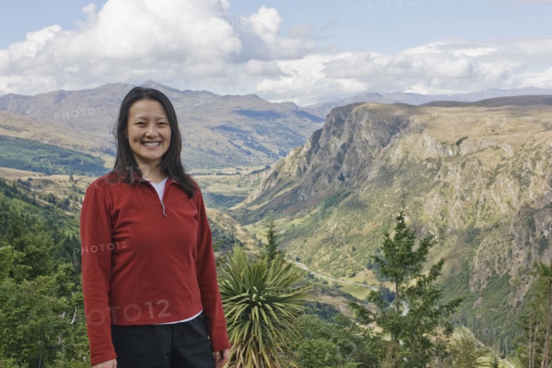 Chinese woman standing on hilltop with remote valley in distance