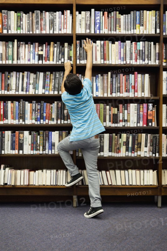 Boy reaching for book on library shelf