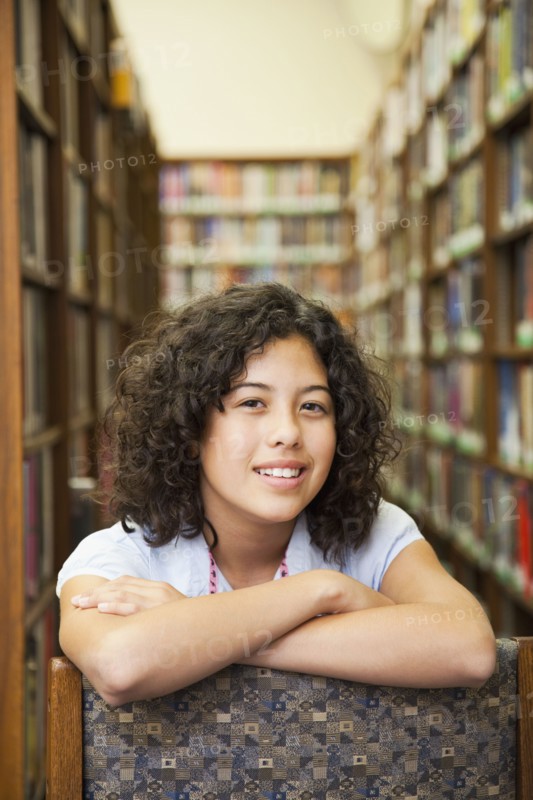 Mixed race girl leaning on chair in library