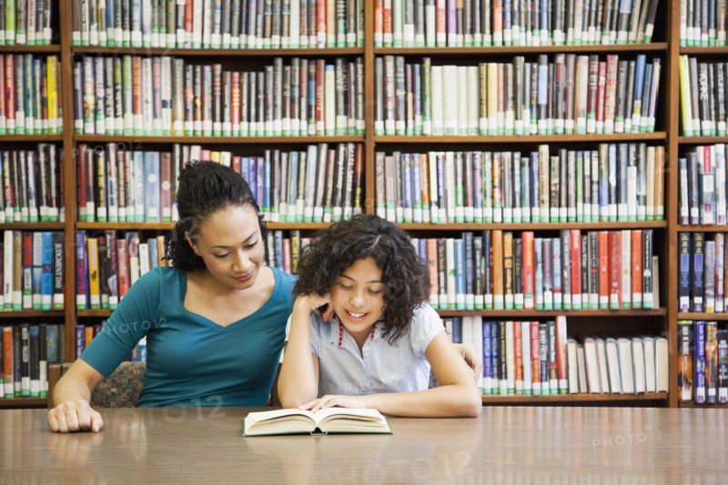 Mother helping daughter read book in library