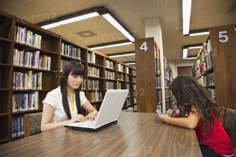 Woman on laptop and girl on video game in library