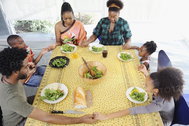 Black family saying grace at dining room table