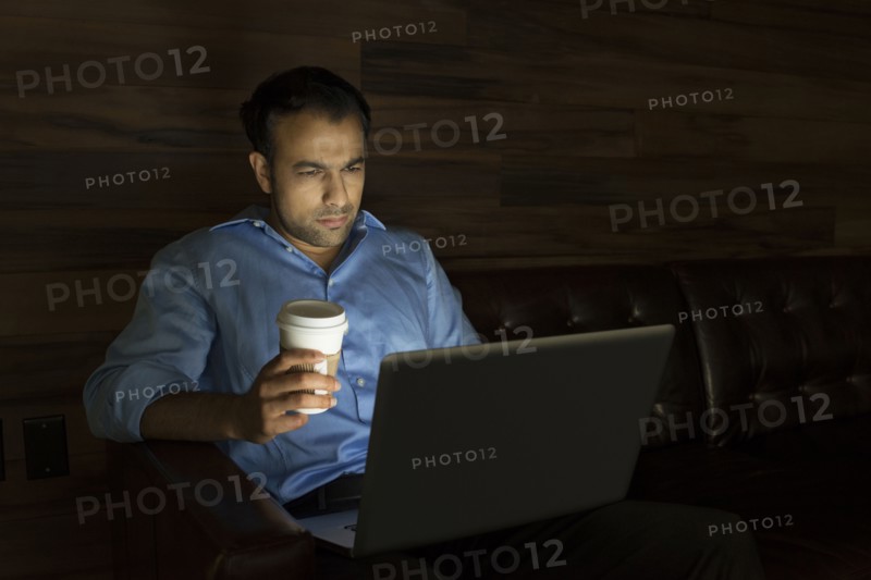 Businessman using laptop on sofa at night