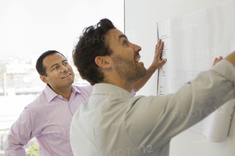 Hispanic businessmen examining blueprints in office