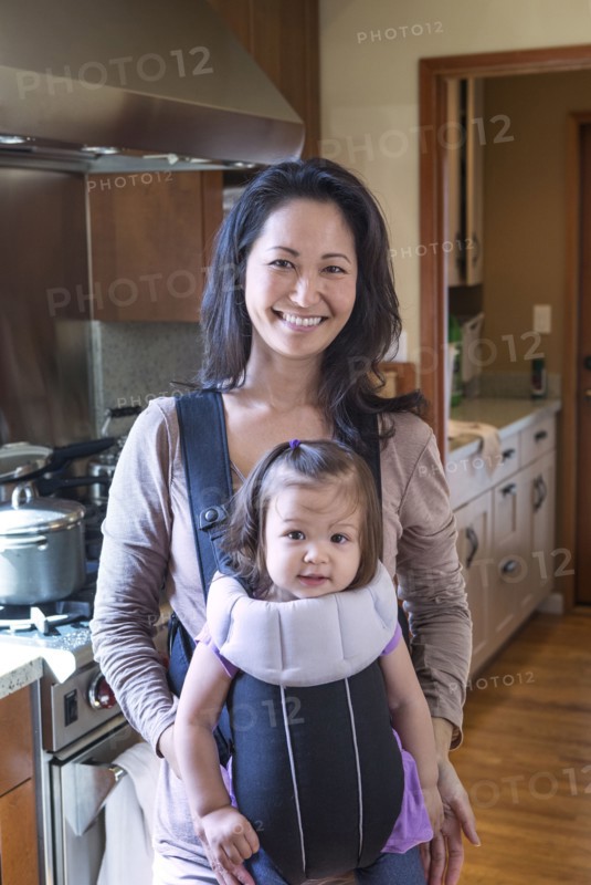 Mother holding daughter in sling in kitchen
