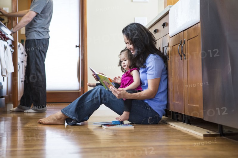Mother reading to daughter in kitchen