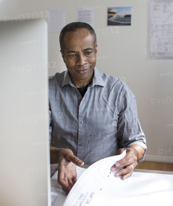 African American architect examining blueprints in office