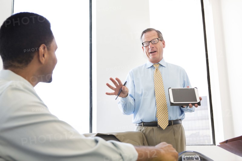Businessman showing digital tablet to colleagues in meeting