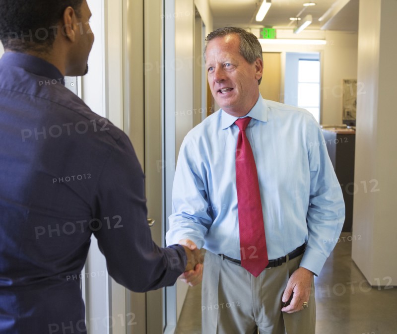 Businessmen shaking hands in office hallway