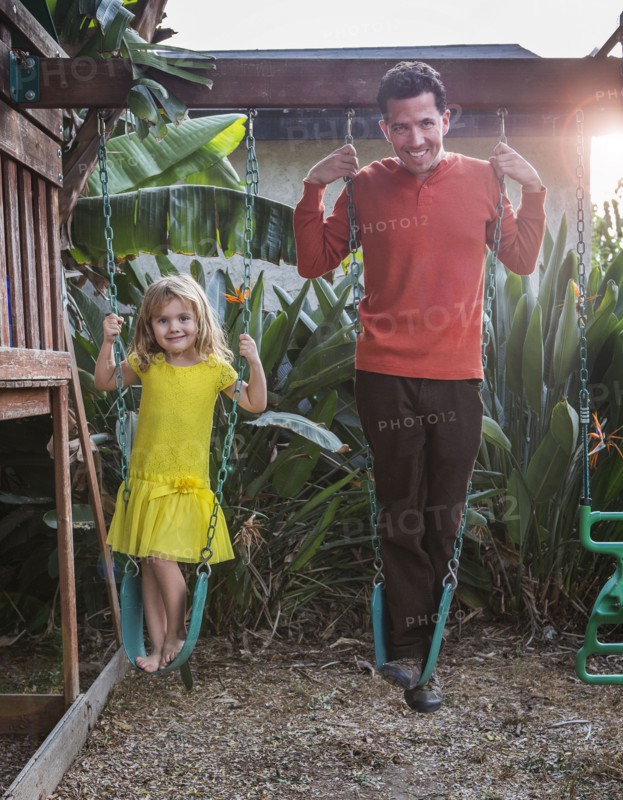 Caucasian father and daughter standing on swings