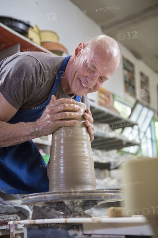 Older Caucasian man forming pottery on wheel in ceramics studio