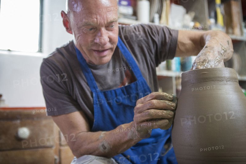 Older Caucasian man forming pottery on wheel in ceramics studio