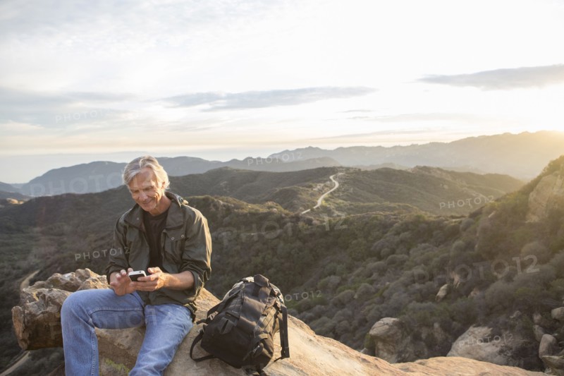 Older Caucasian man using cell phone on rocky hilltop