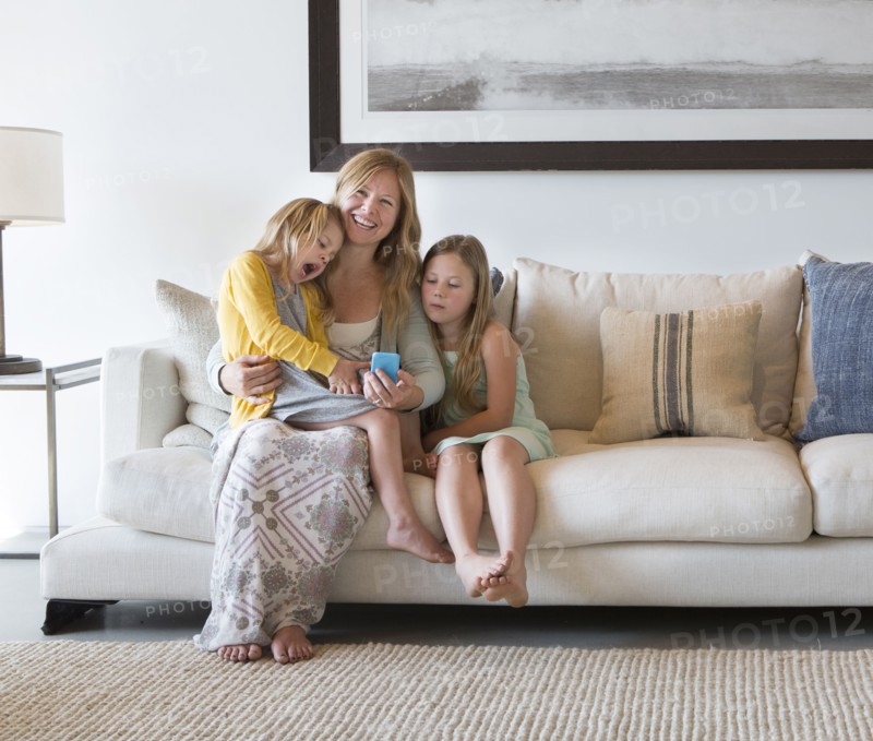 Caucasian mother and daughters using cell phone on sofa