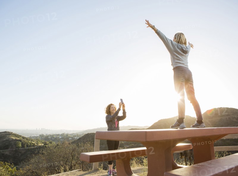 Caucasian woman photographing friend on hilltop