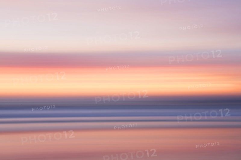 Defocused view of ocean waves on beach under sunset sky