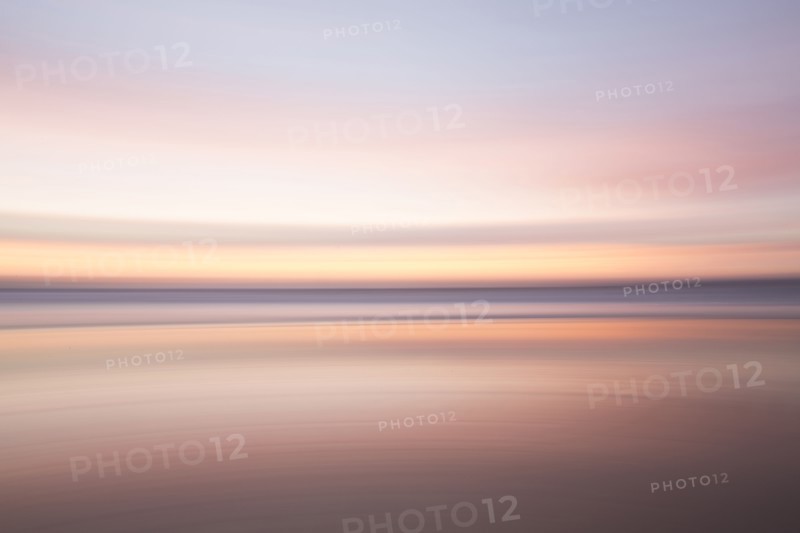Defocused view of ocean waves on beach under sunset sky