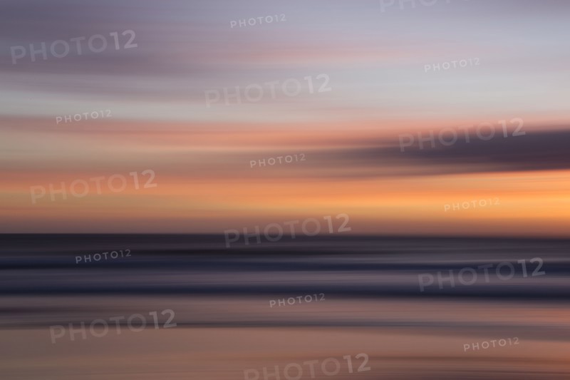 Defocused view of ocean waves on beach under sunset sky