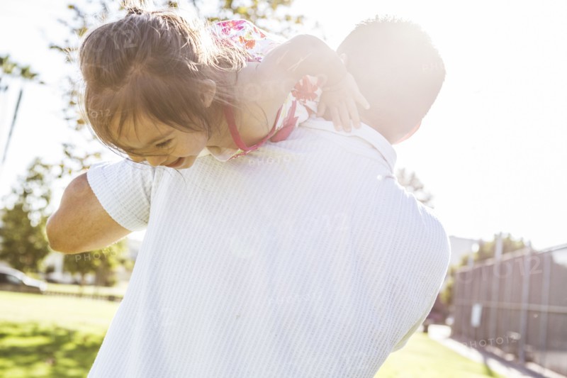 Hispanic father carrying daughter on shoulders