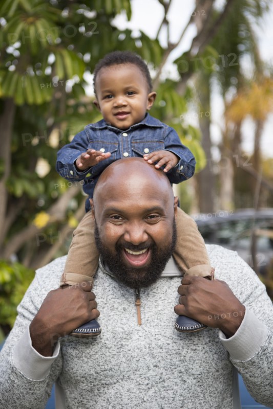 African American father carrying son on shoulders