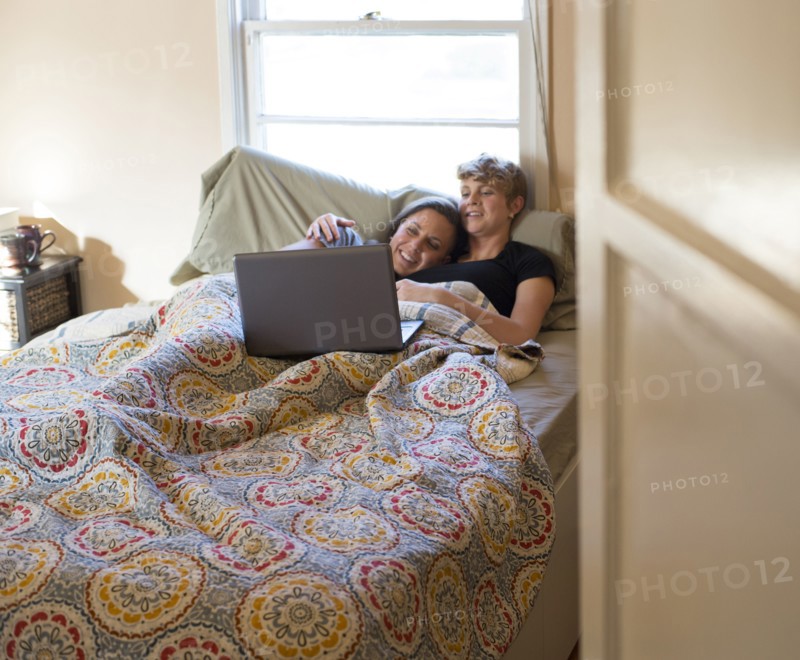 Caucasian lesbian couple watching laptop in bed